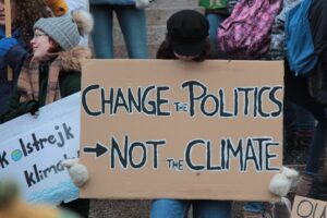 Young person holding cardboard sign that says change the politics not the climate